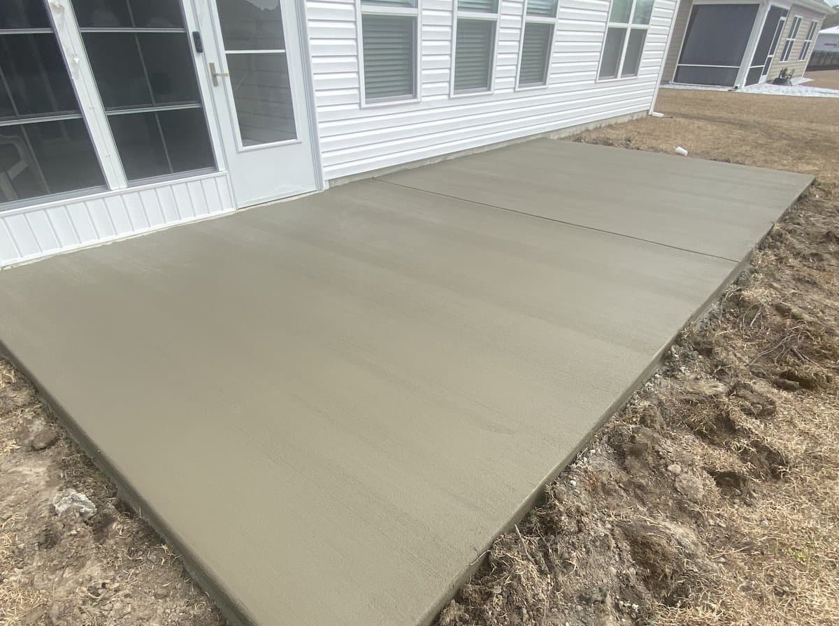 Freshly poured and finished concrete patio slab behind a home